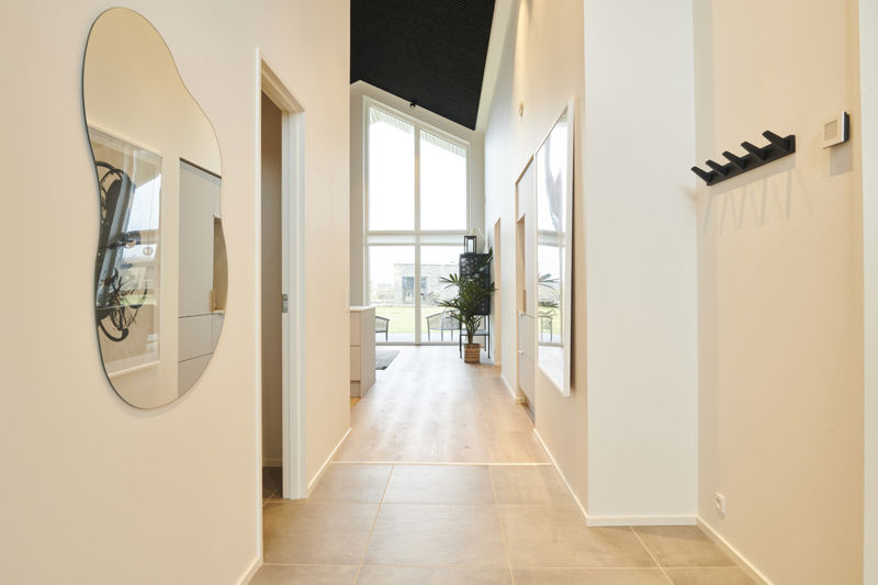 Lys entré fra eurodan-huse med store gulvfliser, organisk spejl, sort knagerække, højt loft, store vinduespartier og kig videre mod opholdsrum – inspiration til rummelig entré, nybyggeri og moderne husbyggeri.