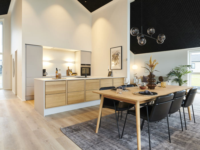 Moderne køkken-alrum i nybyggeri med træfronter, køkkenø, spiseplads, store vinduespartier og akustikloft – inspiration til stilrent husbyggeri.