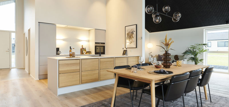 Moderne køkken-alrum i nybyggeri med træfronter, køkkenø, spiseplads, store vinduespartier og akustikloft – inspiration til stilrent husbyggeri.