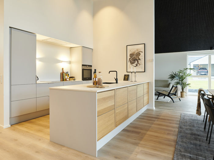 Stilrent køkken i moderne nybyggeri med stor køkkenø, lyse træfronter, integrerede hvidevarer og åben forbindelse til spiseområdet – inspiration til eksklusivt husbyggeri.
