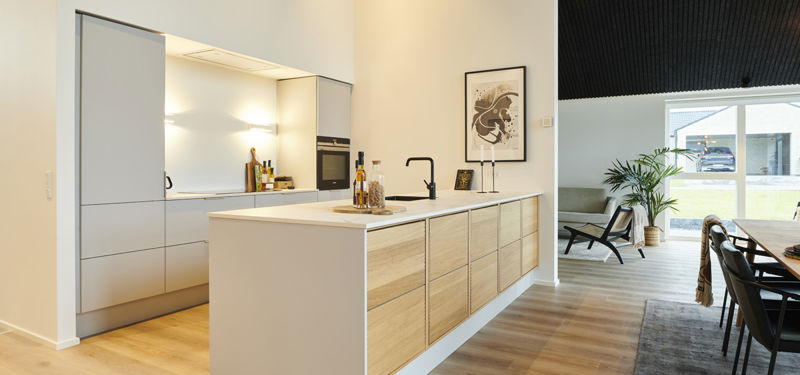 Stilrent køkken i moderne nybyggeri med stor køkkenø, lyse træfronter, integrerede hvidevarer og åben forbindelse til spiseområdet – inspiration til eksklusivt husbyggeri.