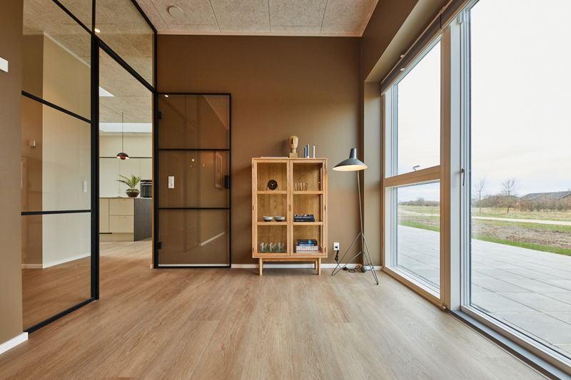 Rum fra eurodan-huse med stort gulv-til-loft vinduesparti, sort indvendig dør med glasfelter, sort rammevæg, træskab og gulvlampe – inspiration til indvendige døre, store vinduer og moderne nybyggeri.