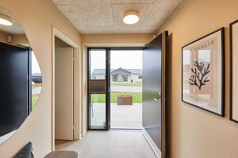 Entré fra eurodan-huse med åben sort hoveddør, stort vinduesparti, lyse gulvfliser, rundt spejl, vægplakater og polstret bænk i hjørnet – inspiration til indbydende nybyggeri, entrédesign og moderne husdrømme.