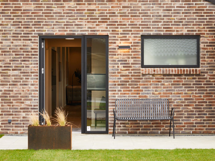 Indgangsparti fra eurodan-huse med rødbrun murstensfacade, sort hoveddør med højt sideparti, smalt vandret vindue, udendørslampe, plantekasse og bænk ved muren – inspiration til døre, entréfacade og nybyggeri med karakter.