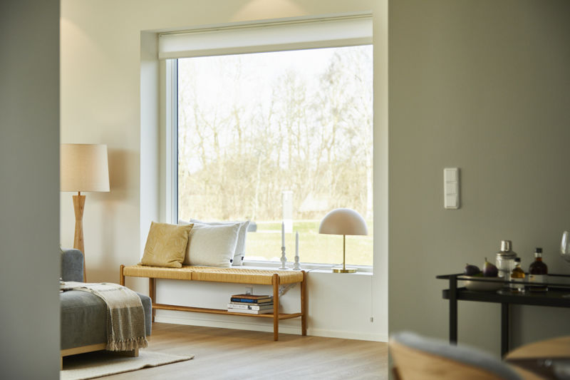 Sansevindue i opholdsrum fra eurodan-huse med bred indbygget bænk, puder, bøger under sædet, bordlampe og stort vindue med udsyn til natur – inspiration til nybyggeri med hyggekrog, lysindfald og gennemtænkte husdrømme.