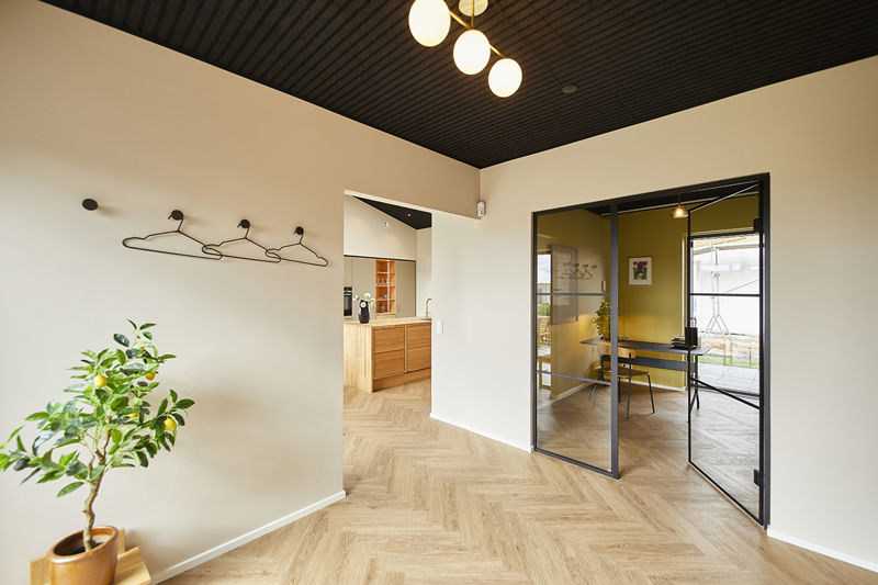 Indgangsområde fra eurodan-huse med sort liste-loft, væghængt knagerække, plante i potte, sildebensgulv, åbning til køkken med træfronter og sort ramme mod kontor – inspiration til entré, nybyggeri og gennemtænkt husbyggeri.