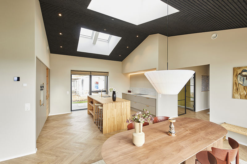 Rummeligt køkken-alrum fra eurodan-huse med træbeklædt køkkenø, barstole, rundt spisebord, hvid pendel, sort loft med ovenlys, lyse sildebensgulve og stor skydedør mod terrasse – inspiration til åbent nybyggeri, funktionelt husbyggeri og køkken-alrum som hjemmets naturlige samlingspunkt.