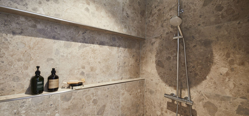 Bruseniche fra eurodan-huse med store marmorerede beige fliser, lang indbygget hylde til shampoo, diskret belysning, brusesæt i krom og glasafskærmning – konkret inspiration til nybyggeri, husbyggeri og praktiske løsninger til badeværelse i nybygget hus.