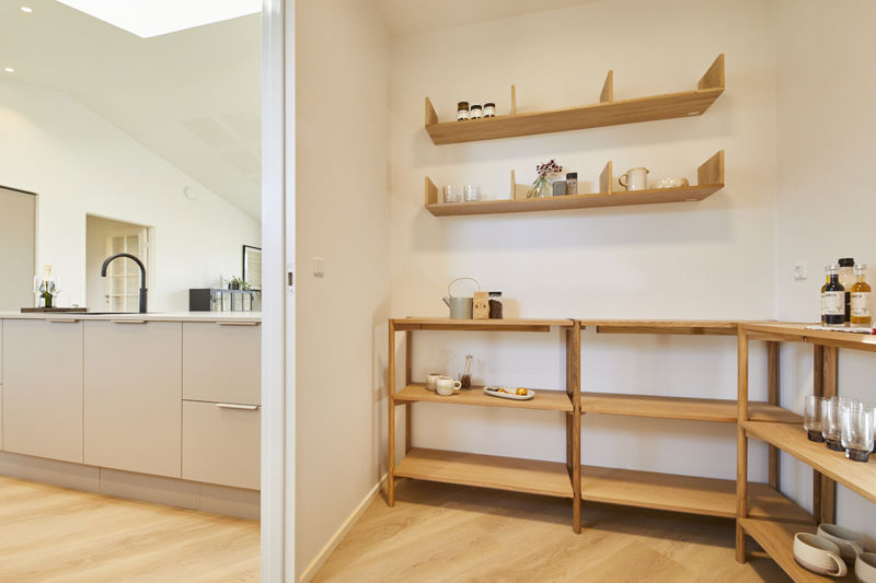 Depotrum ved køkken fra eurodan-huse med åbne træreoler, hylder til glas og tørvarer, træbord langs væggen, flasker og service samt kig ud til køkkenets lyse fronter og sorte armatur – inspiration til praktisk opbevaring i nybyggeri og moderne husdrømme.