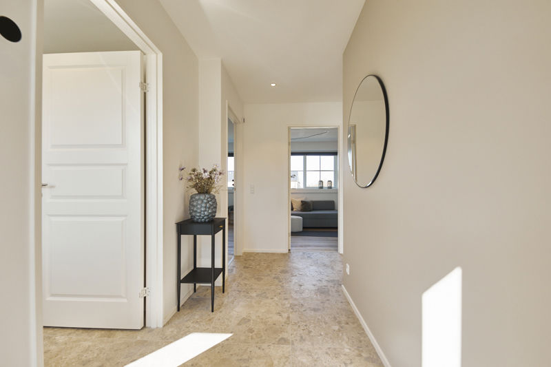 Lys entré fra eurodan-huse med store gulvfliser i naturlook, rundt spejl, smalt sort konsolbord med vase og kig videre til stue – inspiration til enkel entréindretning, nybyggeri og funktionelt husbyggeri.