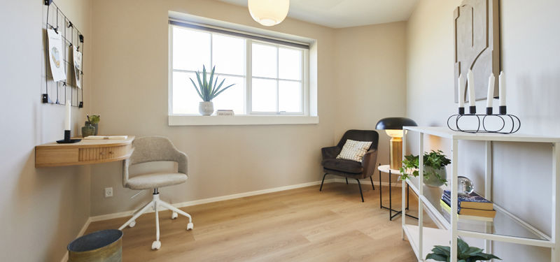 Kontor fra eurodan-huse med væghængt skrivebord i lyst træ, hvid kontorstol, opslagstavle på væggen, stort vindue med plante i karmen, rund loftlampe, loungestol og åben reol med planter og bøger – inspiration til hjemmearbejdsplads i nybyggeri og husbyggeri.