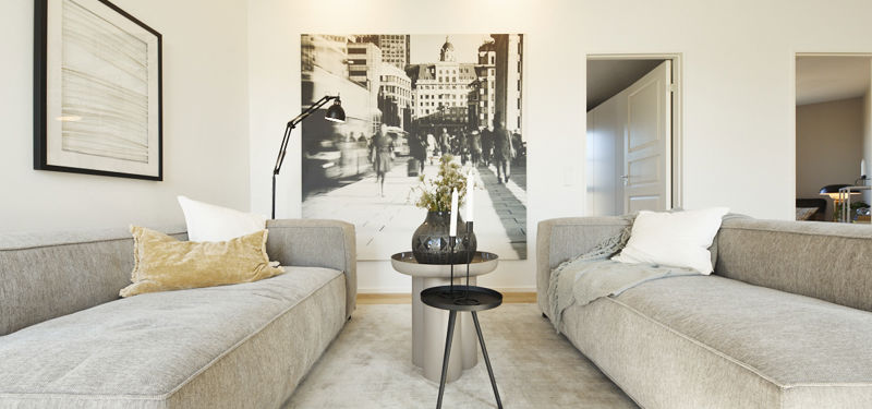 Sofagruppe fra eurodan-huse med to lysegrå sofaer overfor hinanden, rundt sidebord, sort læselampe, stort sort-hvidt billede og lyse vægge – inspiration til roligt opholdsrum, moderne nybyggeri og husdrømme.