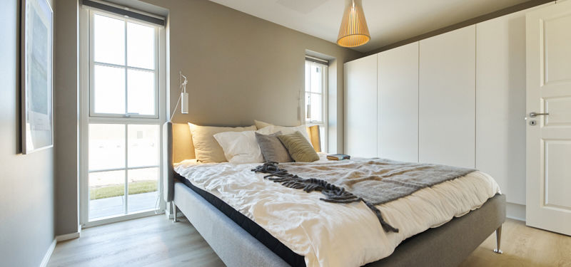 Lyst forældresoveværelse med dobbeltseng, stor indbygget skabsvæg, mørk kontrastvæg og høje sprossevinduer – rolig inspiration til indretningen af drømmehuset.