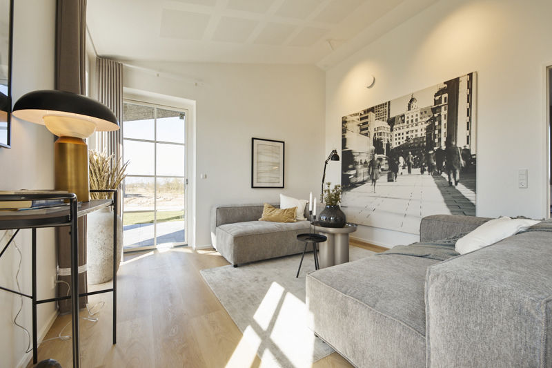 Stue fra eurodan-huse med to grå loungemoduler, rundt sidebord, sort standerlampe, stor sort-hvid vægkunst, lys gulvflade og dobbelte vinduer mod terrasse – inspiration til stilren stue i nybyggeri, husbyggeri og nybygget hus.