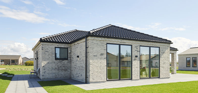 Facade fra eurodan-huse med lyse mursten, sort tegltag, store mørke vinduespartier, terrassedør og flisegang omkring huset – konkret inspiration til placering af vinduer og døre i nybyggeri og moderne husbyggeri.