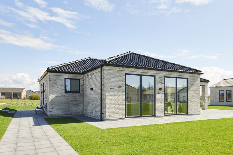 Facade fra eurodan-huse med lyse mursten, sort tegltag, store mørke vinduespartier, terrassedør og flisegang omkring huset – konkret inspiration til placering af vinduer og døre i nybyggeri og moderne husbyggeri.