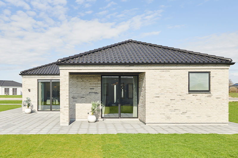 Overdækket terrasse fra eurodan-huse med lys murstensfacade, sort tegltag, glasdøre under tagudhæng, plantekrukker og stor flisebelagt terrasse foran facaden – inspiration til nybyggeri med læfyldt terrasse og funktionelt uderum.