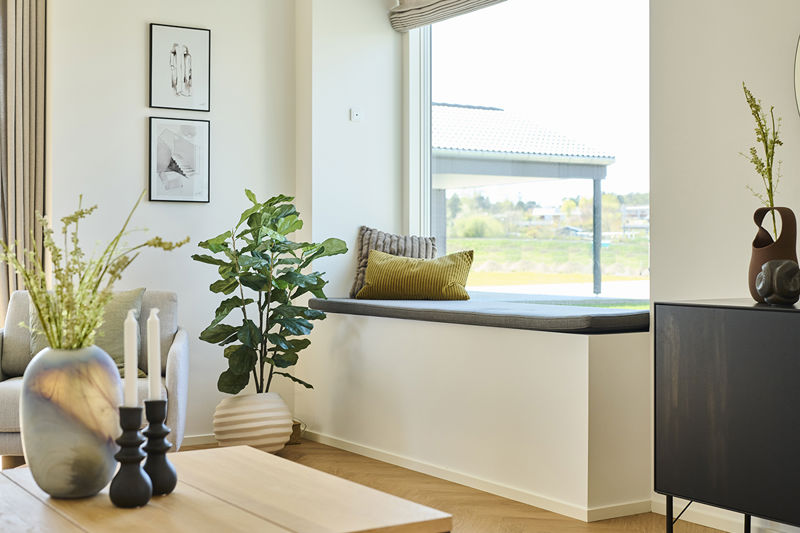 Stue fra eurodan-huse med stort vinduesparti, sansevindue med indbygget siddeplads, beige sofa, rundt sofabord og lange gardiner – inspiration til nybyggeri, husbyggeri og husdrømme med ekstra lys og hyggekrog.