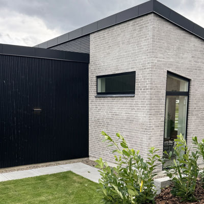 Detalje af moderne facade med lyse mursten, sort træbeklædning og smalle vinduer – inspiration til minimalistisk husbyggeri