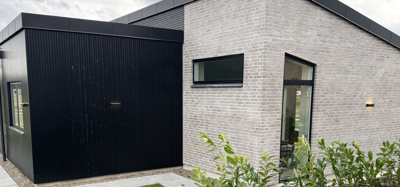 Detalje af moderne facade med lyse mursten, sort træbeklædning og smalle vinduer – inspiration til minimalistisk husbyggeri