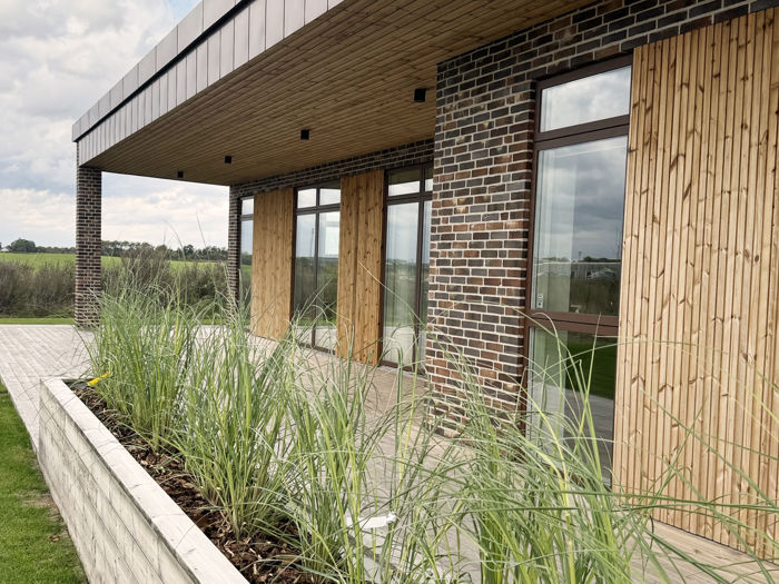 Facade på udstillingshus fra eurodan-huse med træbeklædning, mørke mursten, store vinduer og plantebed til moderne nybyggeri og husbyggeri.