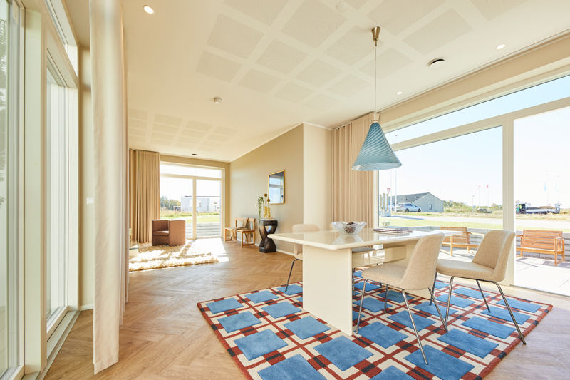 Lys spisestue i moderne nybyg med store gulv-til-loft-vinduer, hvidt spisebord, polstrede stole og blå pendel – inspiration til drømmehuset.
