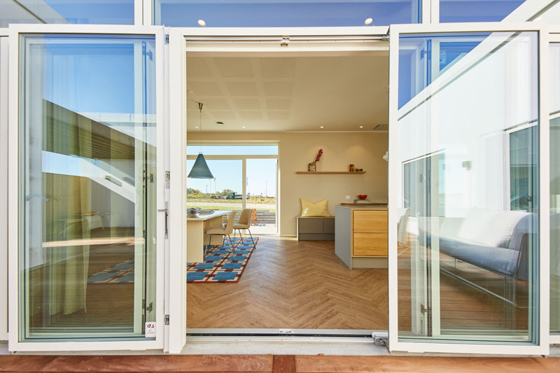 Åbne dobbeltdøre fra terrasse ind til køkken-alrum fra eurodan-huse med stort lysindfald, spiseplads, køkkenø i trælook, sansevindue med hynde og brede vinduesrammer – inspiration til nybyggeri og husdrømme med inde-ude forbindelse.