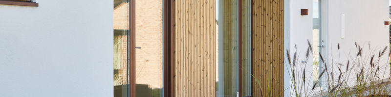Moderne indgangsparti med lodret træbeklædning, store glaspartier, flisebelægning, væglamper og plantekasse i rustlook – stilren inspiration til nybyg og husdrømme.