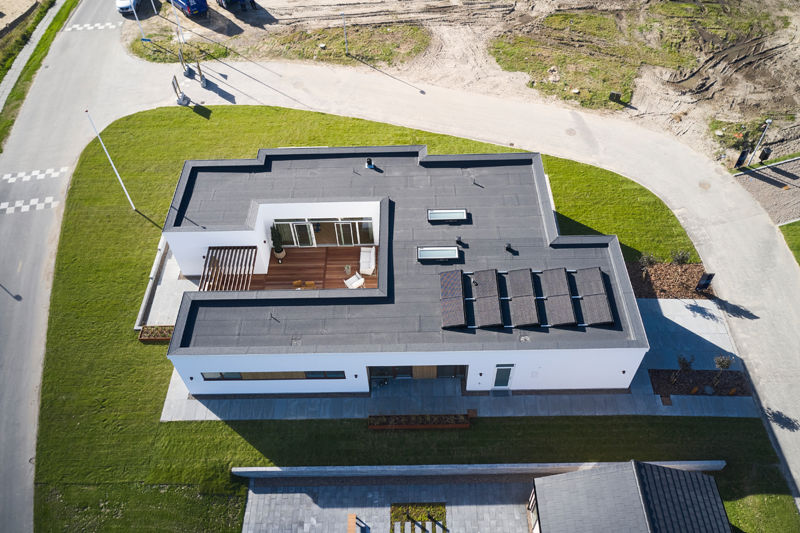 Dronefoto af moderne nybyg med fladt tag, solceller, ovenlys og central atriumgård med træterrasse – inspiration til nyt hus og husdrømme.