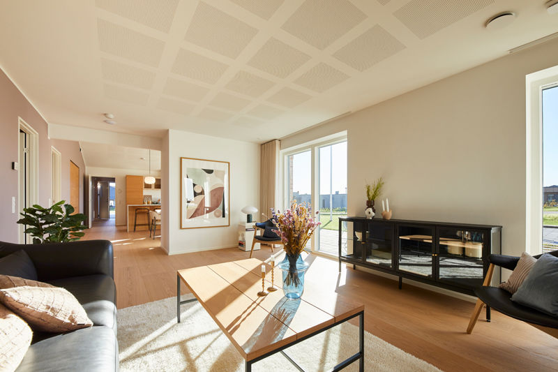 Stue fra eurodan-huse med mørk sofa, lyst sofabord med glasplade, sort vitrineskab, stor plakat på væggen, store vinduer mod terrasse og kig videre til køkken-alrum – inspiration til moderne nybyggeri, husbyggeri og husdrømme.