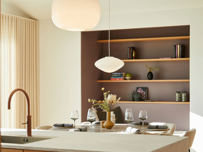 Detalje fra lyst køkken-alrum i moderne nybyg med pendellamper, dækket spisebord og indbyggede træhylder – inspiration til indretning af drømmehuset.