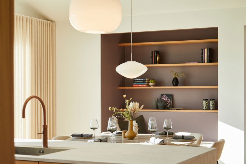 Detalje fra lyst køkken-alrum i moderne nybyg med pendellamper, dækket spisebord og indbyggede træhylder – inspiration til indretning af drømmehuset.