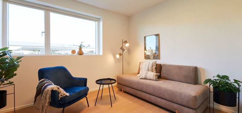 Lyst værelse i nybyg med sovesofa, blå loungestol, gulvlampe og stort vindue – inspiration til gæsteværelse eller ekstra opholdsrum i et nyt hus.