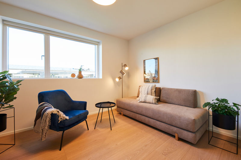 Lyst værelse i nybyg med sovesofa, blå loungestol, gulvlampe og stort vindue – inspiration til gæsteværelse eller ekstra opholdsrum i et nyt hus.