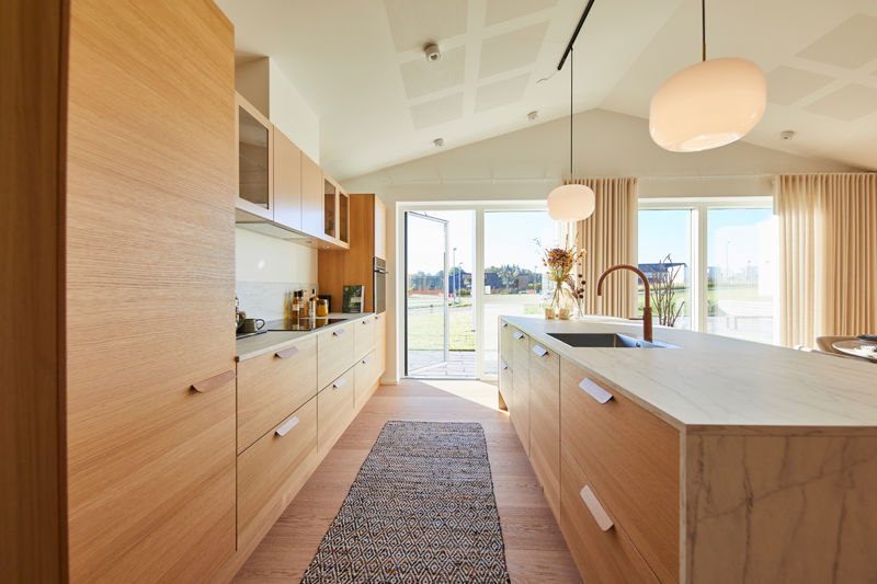Moderne køkken i nybyg med gennemgående træfronter, rummelig køkkenø, lyst bordplade og udgang til haven – inspiration til drømmehuset.