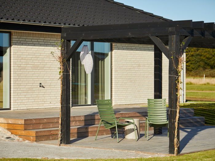Terrasse fra eurodan-huse med sort pergola, trædæk, grønne havestole, lyse mursten, store vinduespartier og klatreplanter på pergolastolperne – inspiration til hyggeligt uderum, nybyggeri og husdrømme med terrasse.