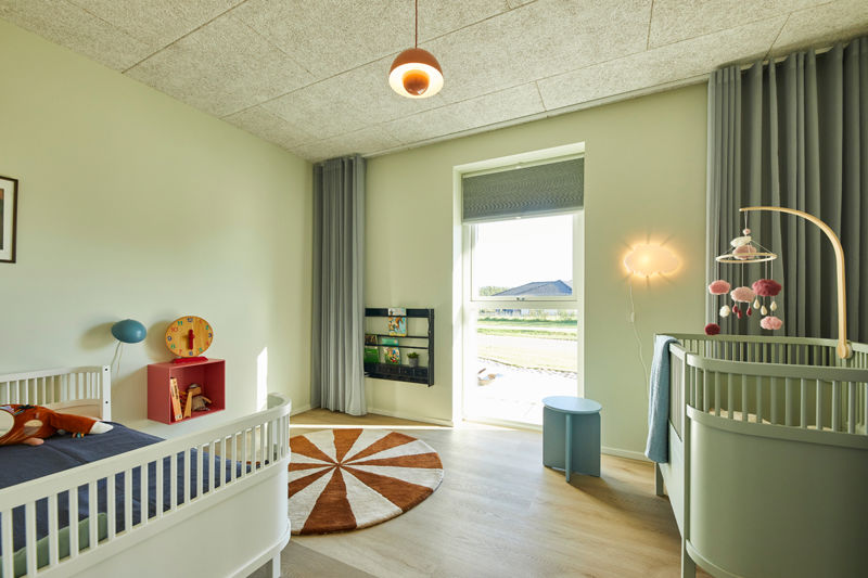 Lyst børneværelse i nybyggeri med tremmesenge, stort vindue, gardiner og moderne indretning – inspiration til familiens husdrømme.
