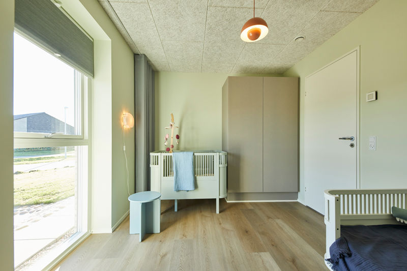 Lyst børneværelse i nybyggeri med tremmeseng, stort gulv-til-loft-vindue, garderobeskab og rolig indretning – inspiration til familiens nye hus.