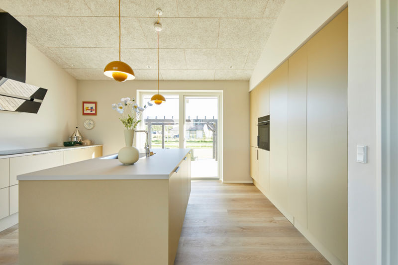 Stilrent køkken i nybyggeri med stor køkkenø, integrerede hvidevarer, pendler og direkte udgang til terrassen – inspiration til moderne husbyggeri.