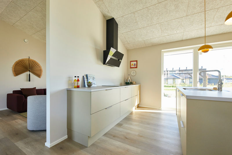 Stilrent køkken i nybyggeri med lyse fronter, køkkenø, sort emhætte og store vinduespartier – moderne inspiration til husbyggeri og personlige husdrømme.