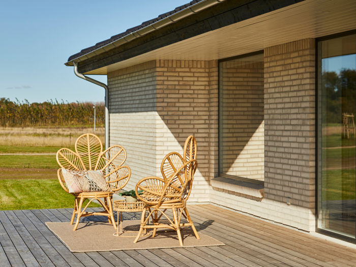 Træterrasse ved moderne længehus i nybyggeri med lys murstensfacade, store vinduespartier og hyggelig spiseplads – inspiration til udeliv og nye husdrømme.