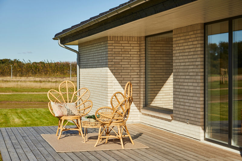 Træterrasse ved moderne længehus i nybyggeri med lys murstensfacade, store vinduespartier og hyggelig spiseplads – inspiration til udeliv og nye husdrømme.