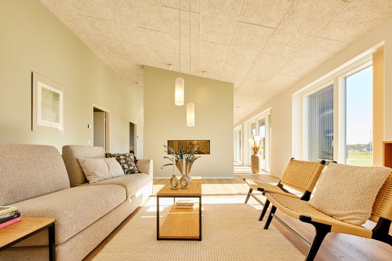 Stue fra eurodan-huse med lang beige sofa, to flettede loungestole, smalt sofabord med vaser, lyse gulve, højt loft og store vinduespartier med naturligt lys – konkret inspiration til nybygget hus, nybyggeri og indretning af stue.