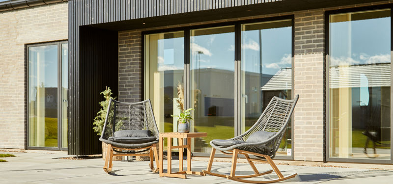 Overdækket terrasse med loungestole foran store glaspartier i moderne nybyggeri – skabt til udeliv og husdrømme hos eurodan-huse