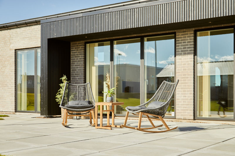 Overdækket terrasse med loungestole foran store glaspartier i moderne nybyggeri – skabt til udeliv og husdrømme hos eurodan-huse