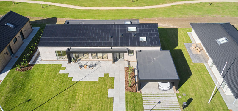 Dronefoto af moderne længehus med solcelletag, overdækket terrasse og integreret carport – inspiration til nybyggeri og husdrømme med eurodan-huse