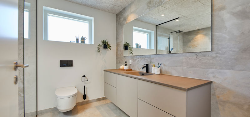 Moderne badeværelse med stort spejl, væghængt toilet og højtsiddende vindue – gennemtænkt husbyggeri med eurodan-huse