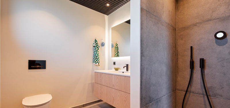 Moderne badeværelse med væghængt toilet, badmøbel i lyst træ, stort spejl og bruseniche med store grå fliser, sorte armaturer og mørkt listeloft – stilren inspiration til nybyg og husdrømme.