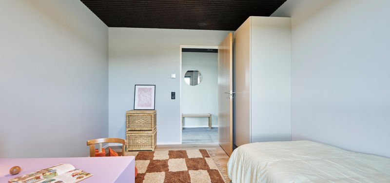 Børneværelse fra eurodan-huse med lys seng, pink børnebord, flettet kommode, stort skab, mørkt loft og åben dør mod gang – inspiration til ekstra værelser, børneindretning og praktiske løsninger i nybyggeri.