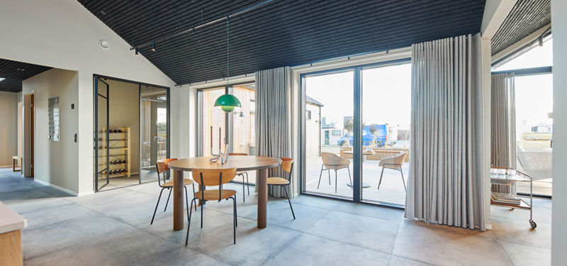 Spiseplads i åbent køkken-alrum med store skydedøre til terrasse, sort akustikloft og vinrum med New Yorker-døre i nybygget barnhouse